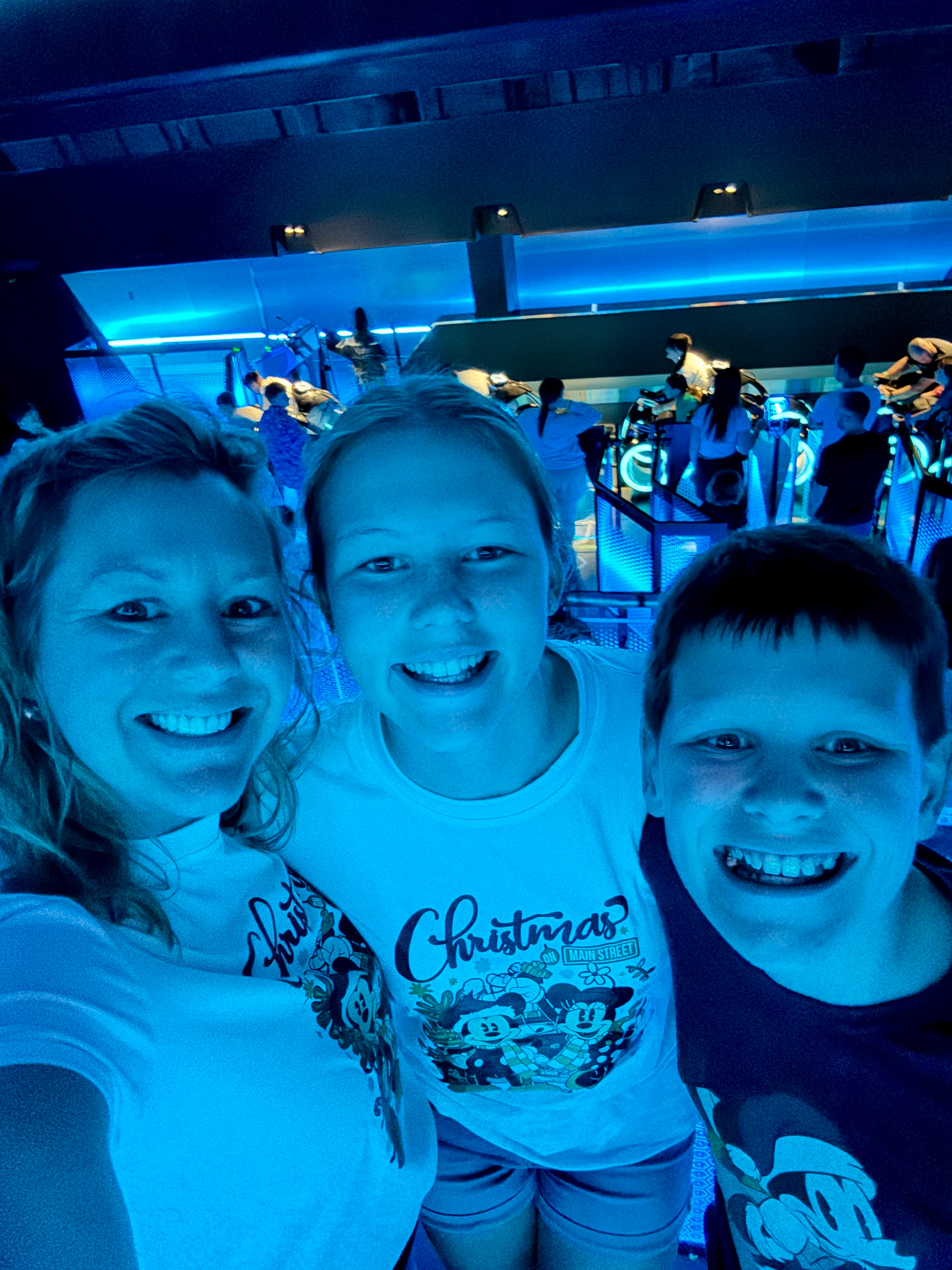 Mom and two teenagers smiling together inside TRON Lightcycle Run at Magic Kingdom.