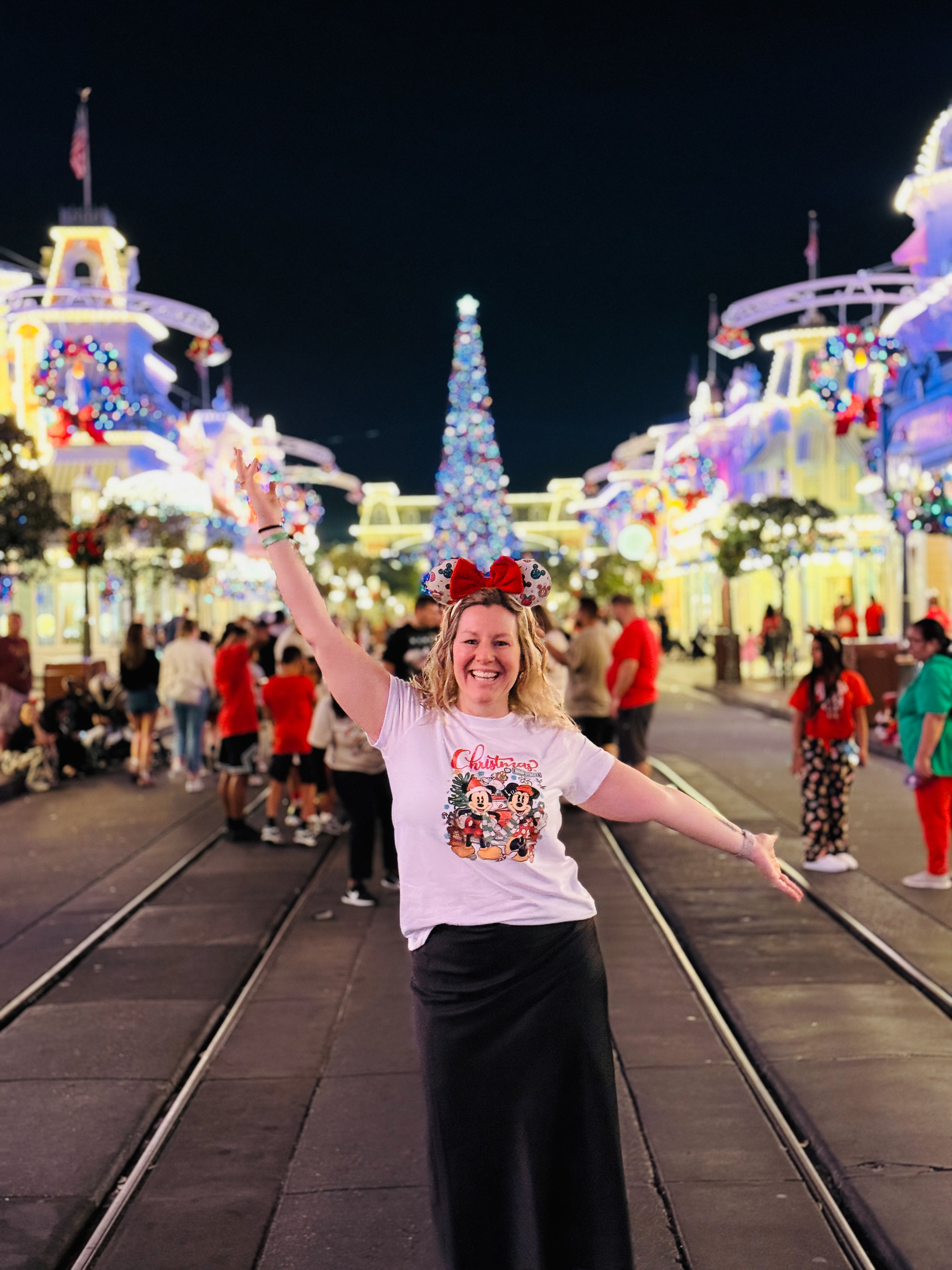 Woman smiling with arms out on Main Street U.S.A. during Mickey’s Very Merry Christmas Party.