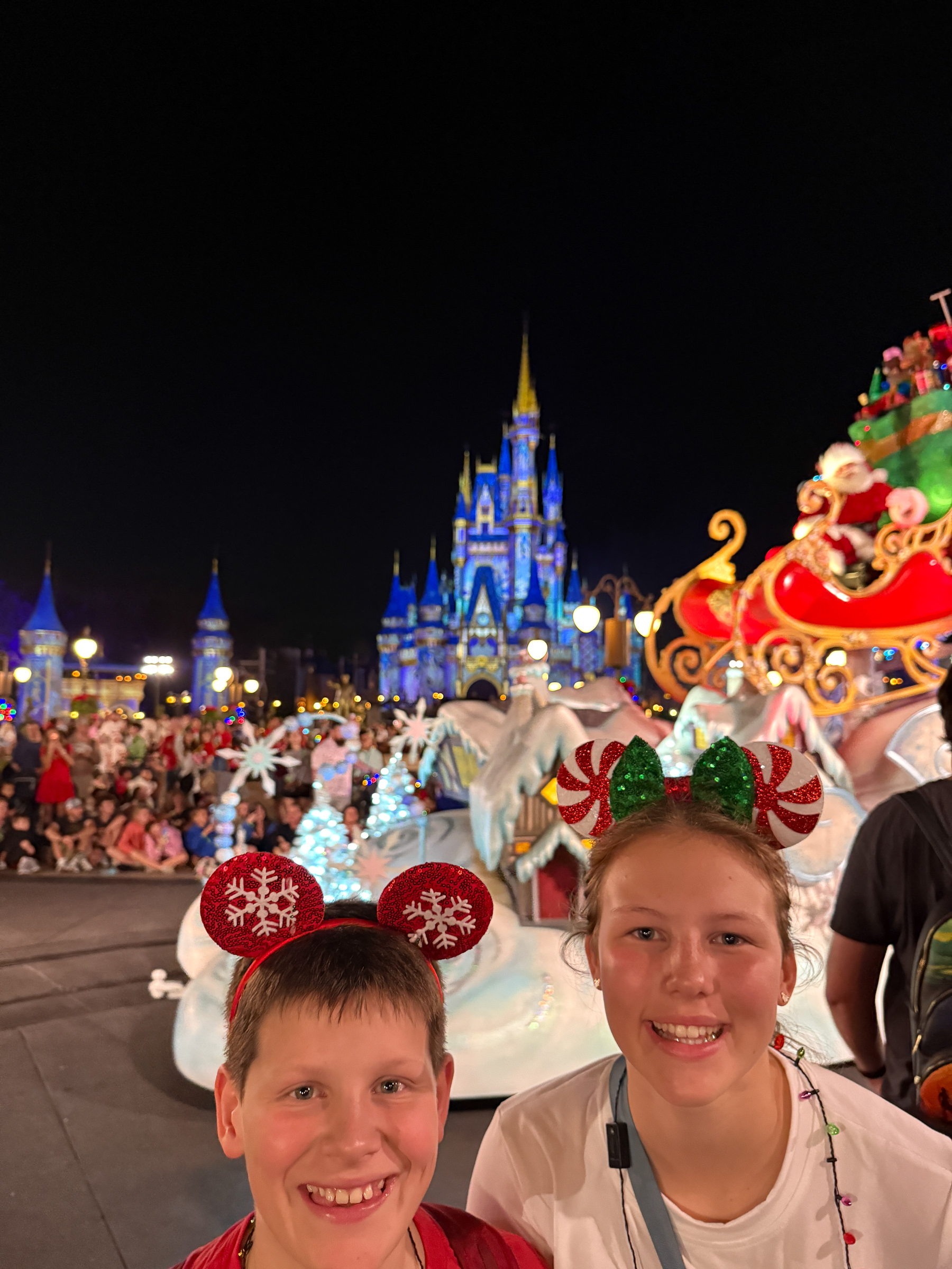 Two teenagers smiling beside Santa’s sleigh during Mickey’s Once Upon a Christmastime Parade.