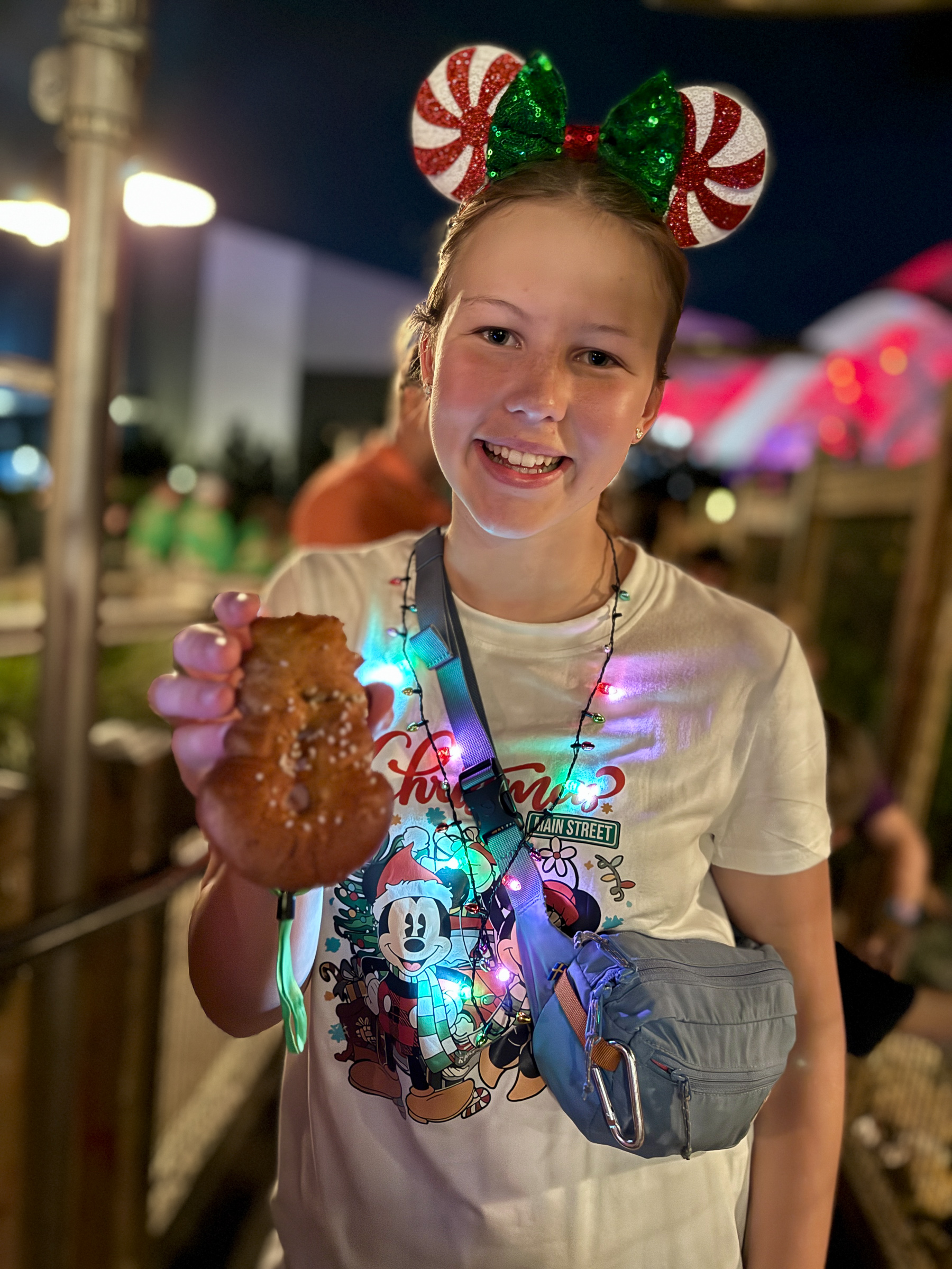 Teen girl holding a snowman-shaped pretzel during Mickey’s Very Merry Christmas Party.