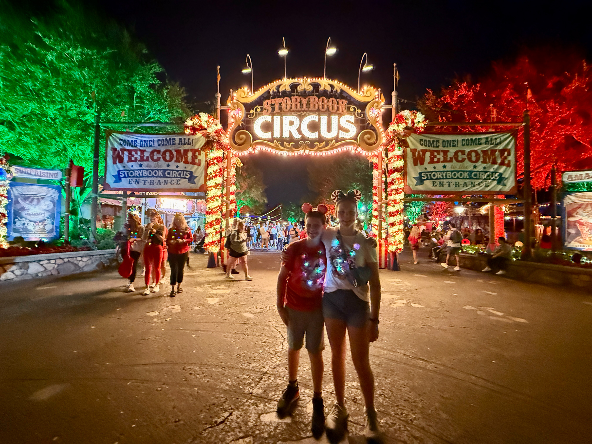 Two teenagers standing beneath the decorated Storybook Circus entrance during Mickey’s Very Merry Christmas Party.