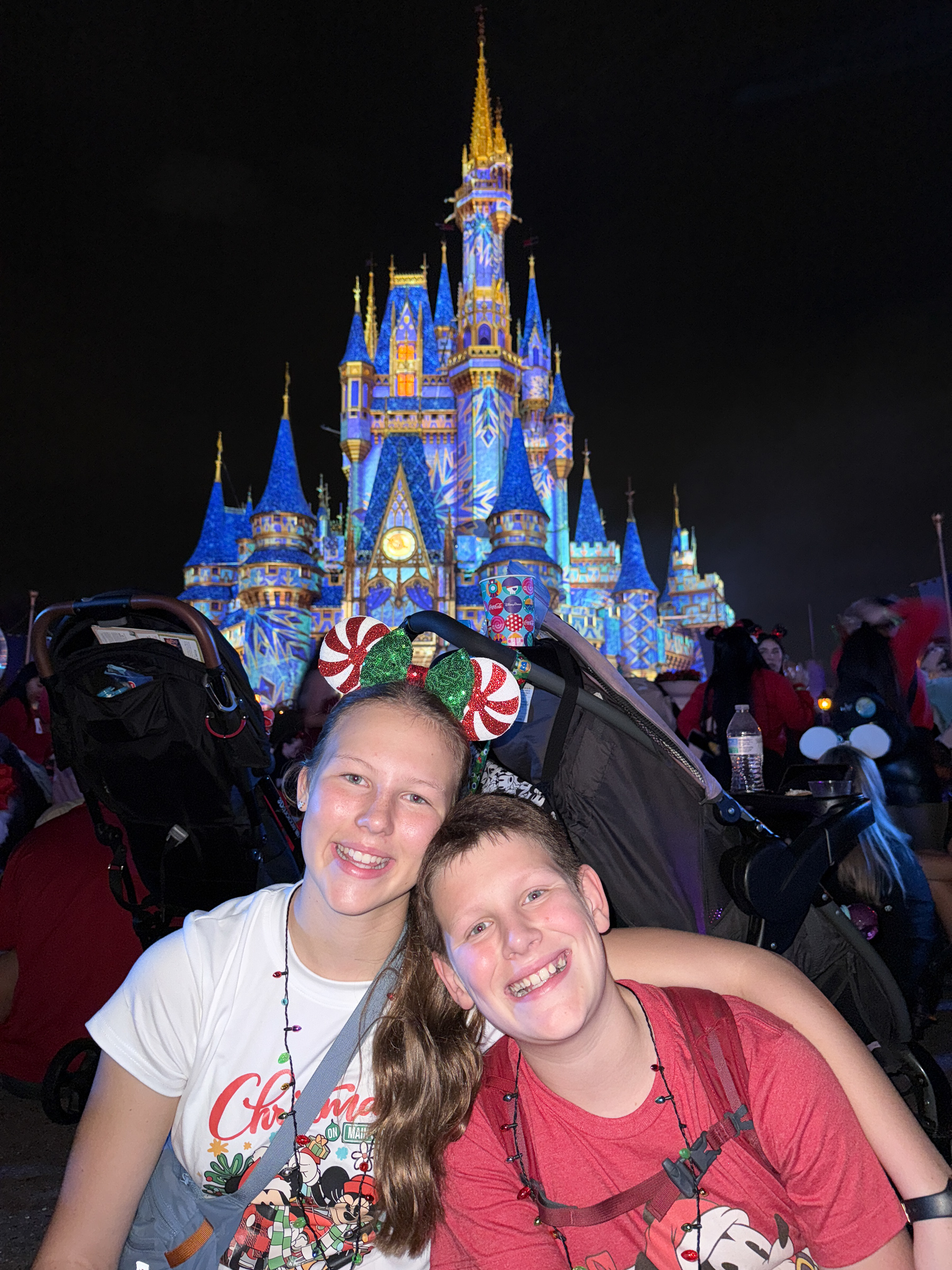 Teen siblings smiling together in front of Cinderella Castle during Mickey’s Very Merry Christmas Party.