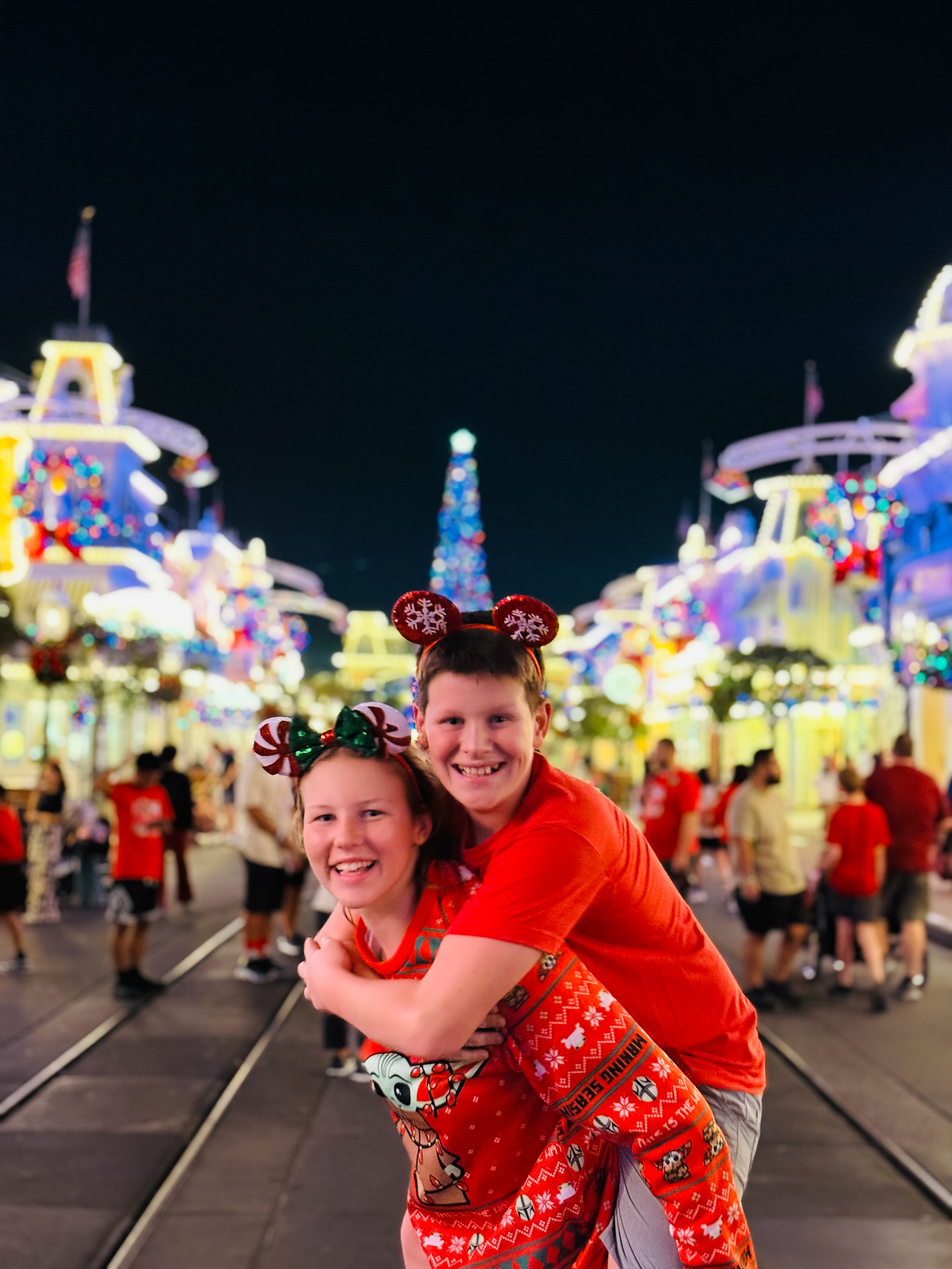 Teen siblings hugging on Main Street U.S.A. with the Christmas tree and holiday lights behind them.