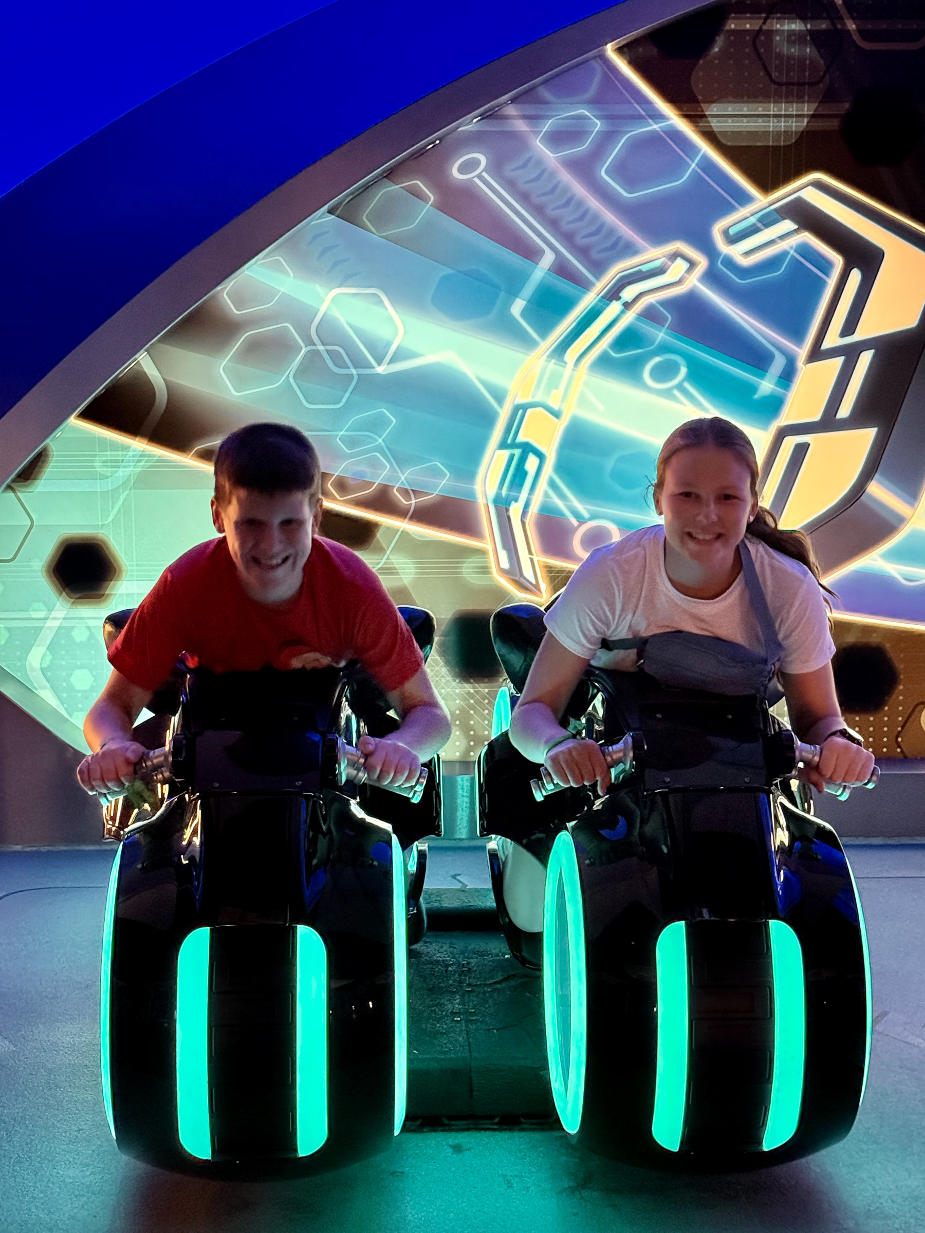 Two teenagers seated on TRON Lightcycle Run motorcycles at Magic Kingdom.